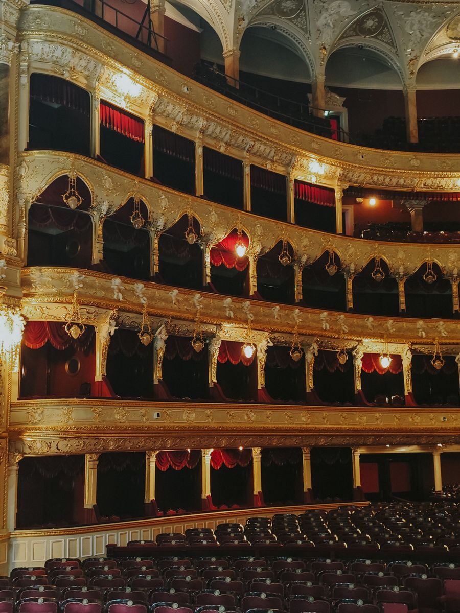 Luxurious opera house interior featuring ornate gold designs and red velvet balconies.