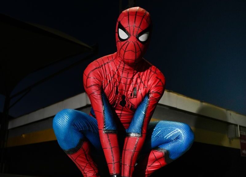 A person in Spider-Man costume crouching outdoors at night, poised for action.