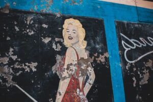 Colorful graffiti of famous woman in red dress on weathered black wall with blue lines of building of town