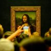 Crowd admiring the Mona Lisa painting at the Louvre Museum in Paris with phones capturing the moment.