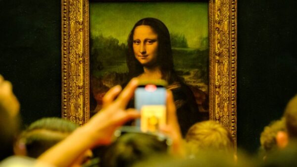 Crowd admiring the Mona Lisa painting at the Louvre Museum in Paris with phones capturing the moment.