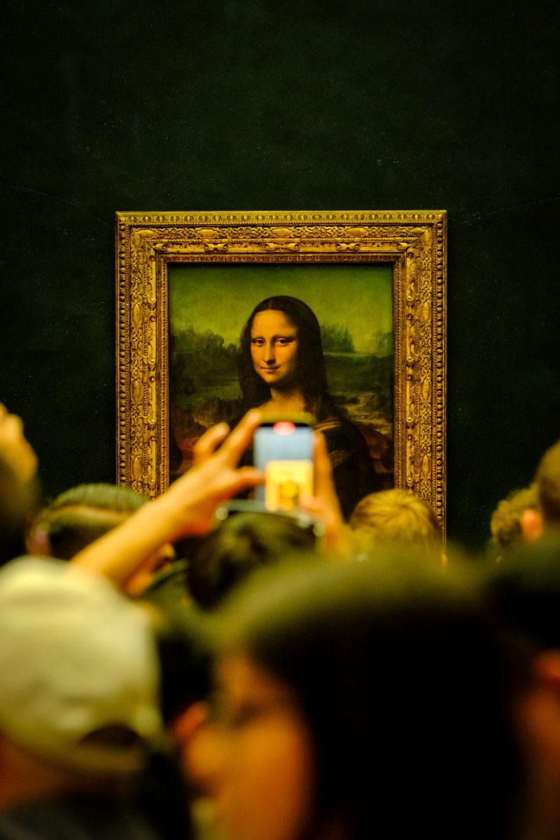 Crowd admiring the Mona Lisa painting at the Louvre Museum in Paris with phones capturing the moment.
