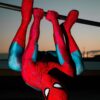 A superhero in red and blue costume hangs upside down on bars at sunset.
