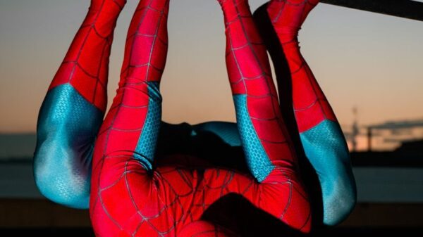 A superhero in red and blue costume hangs upside down on bars at sunset.
