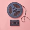 A vintage cassette and film reel placed on a pastel pink background in a flat lay composition.