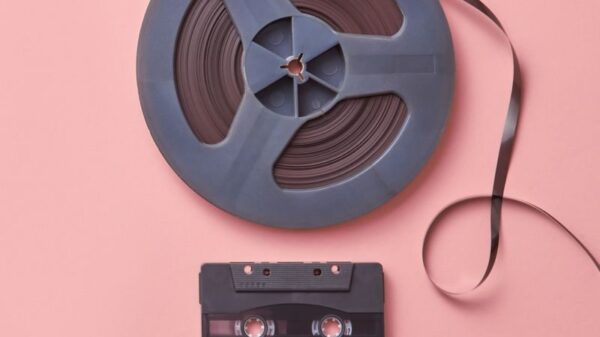 A vintage cassette and film reel placed on a pastel pink background in a flat lay composition.