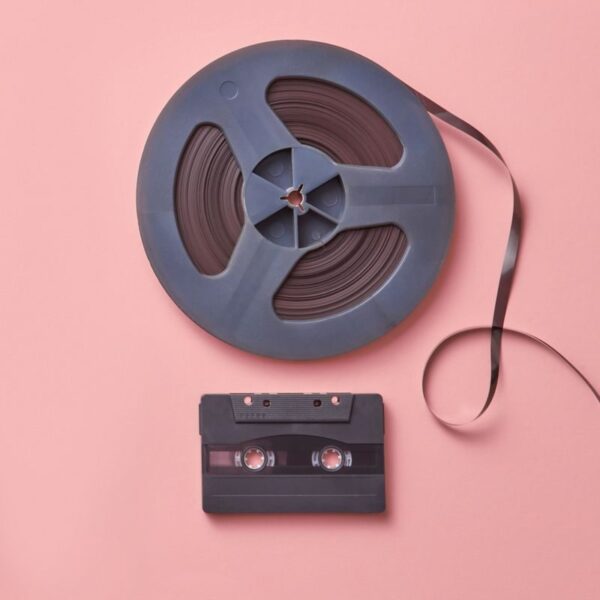 A vintage cassette and film reel placed on a pastel pink background in a flat lay composition.