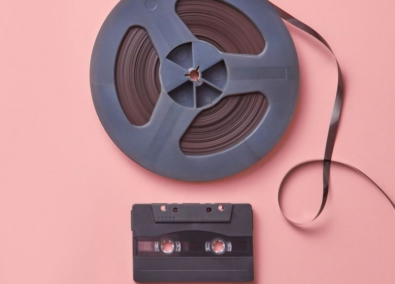 A vintage cassette and film reel placed on a pastel pink background in a flat lay composition.