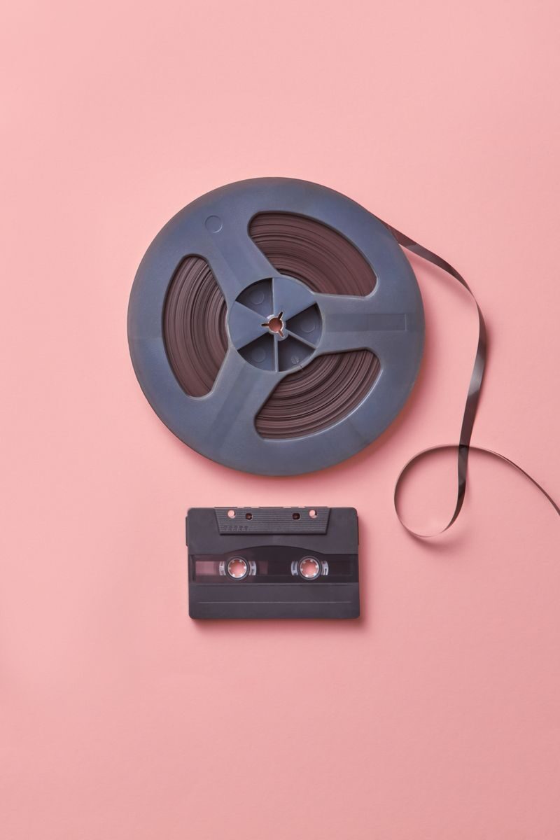 A vintage cassette and film reel placed on a pastel pink background in a flat lay composition.
