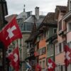 Colorful street in Zurich adorned with Swiss flags under a cloudy sky, showcasing Swiss culture and architecture.