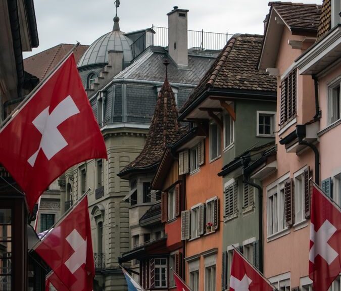 Colorful street in Zurich adorned with Swiss flags under a cloudy sky, showcasing Swiss culture and architecture.