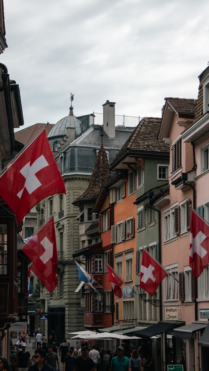 Colorful street in Zurich adorned with Swiss flags under a cloudy sky, showcasing Swiss culture and architecture.