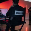 Director sits on chair in moody film studio, overseeing production setup.