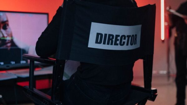 Director sits on chair in moody film studio, overseeing production setup.