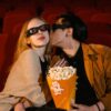 Young couple enjoying a movie date with popcorn in a theater, wearing 3D glasses.