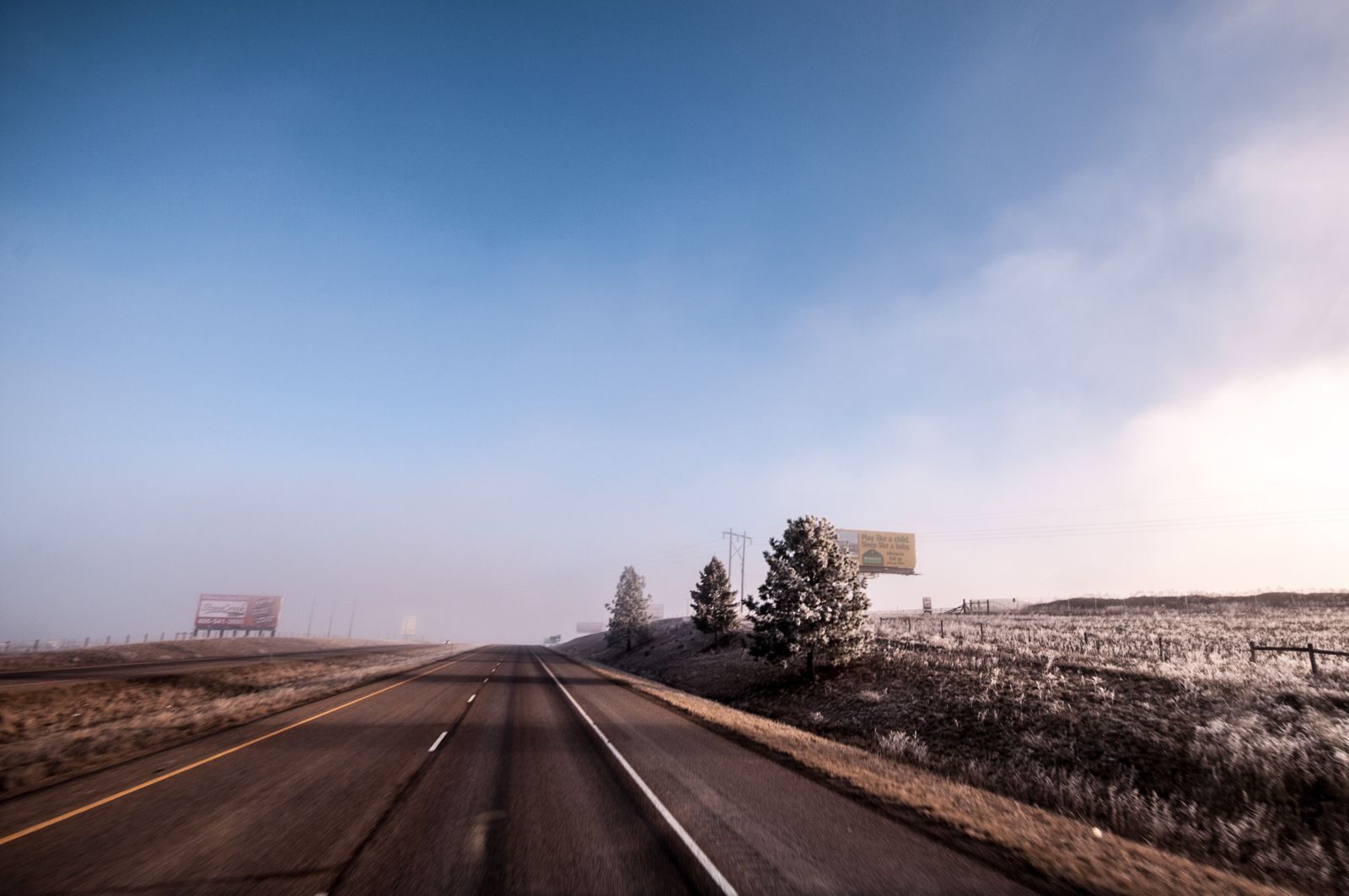 Open highway on a frosty winter morning with clear blue skies and distant billboards.
