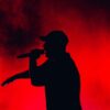 Silhouette of a performer singing on stage with striking red and black lighting.