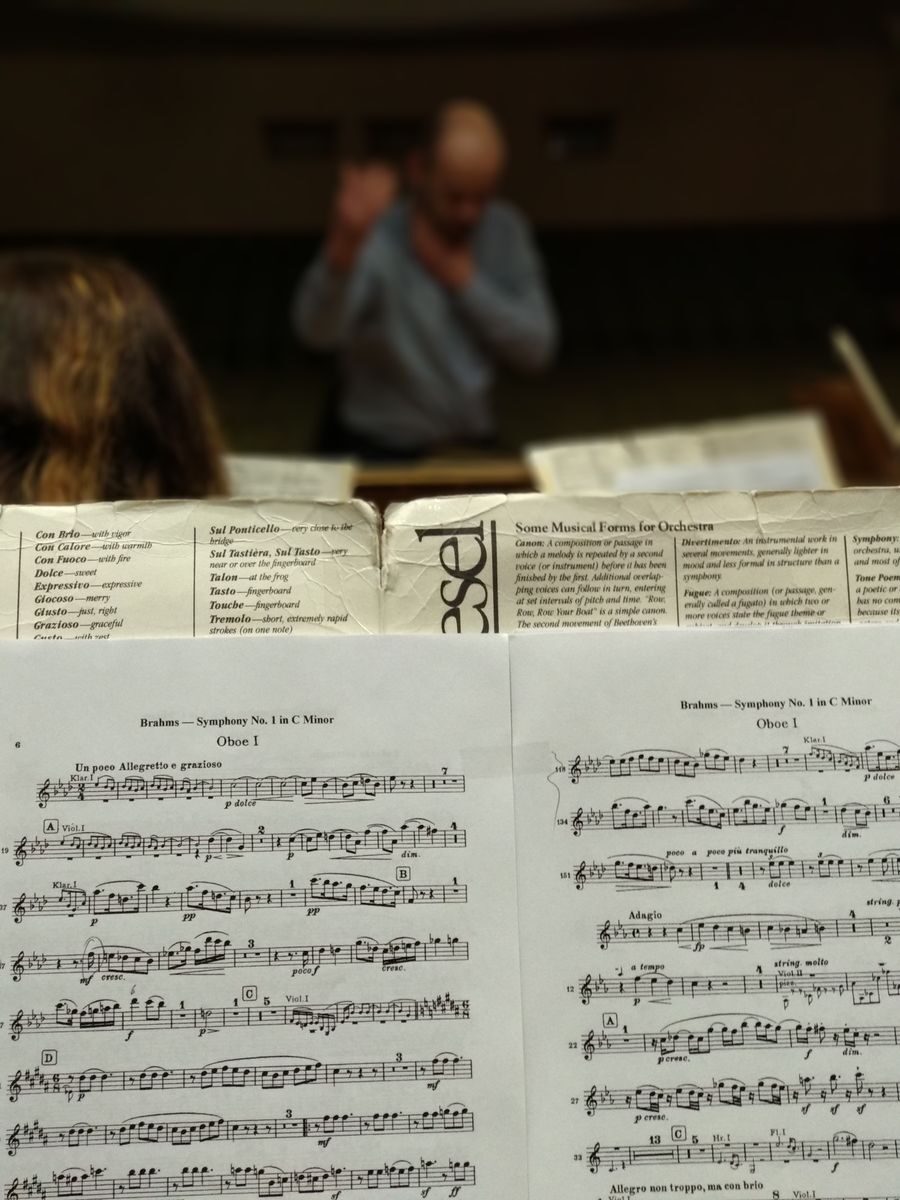 Detailed shot of sheet music during a symphony rehearsal, conductor in the background.
