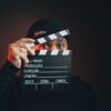 Portrait of a man holding a clapperboard with a dramatic dark background.