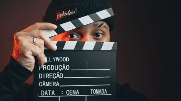 Portrait of a man holding a clapperboard with a dramatic dark background.