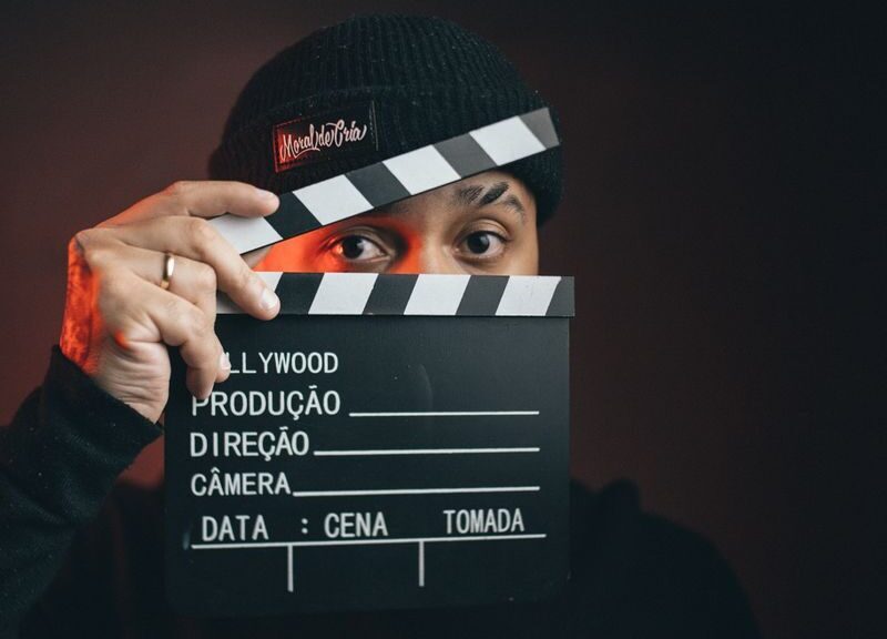 Portrait of a man holding a clapperboard with a dramatic dark background.