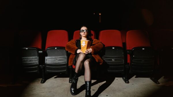 A stylish woman sits alone in a dark cinema, enjoying popcorn during a movie.