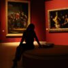 Silhouetted visitor in an art gallery with dramatic lighting on classic paintings.