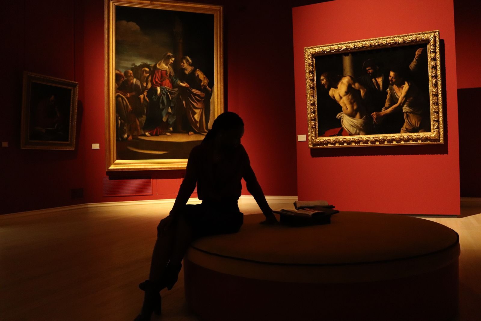 Silhouetted visitor in an art gallery with dramatic lighting on classic paintings.