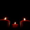 Moody and serene image of three red candles burning softly in the dark.