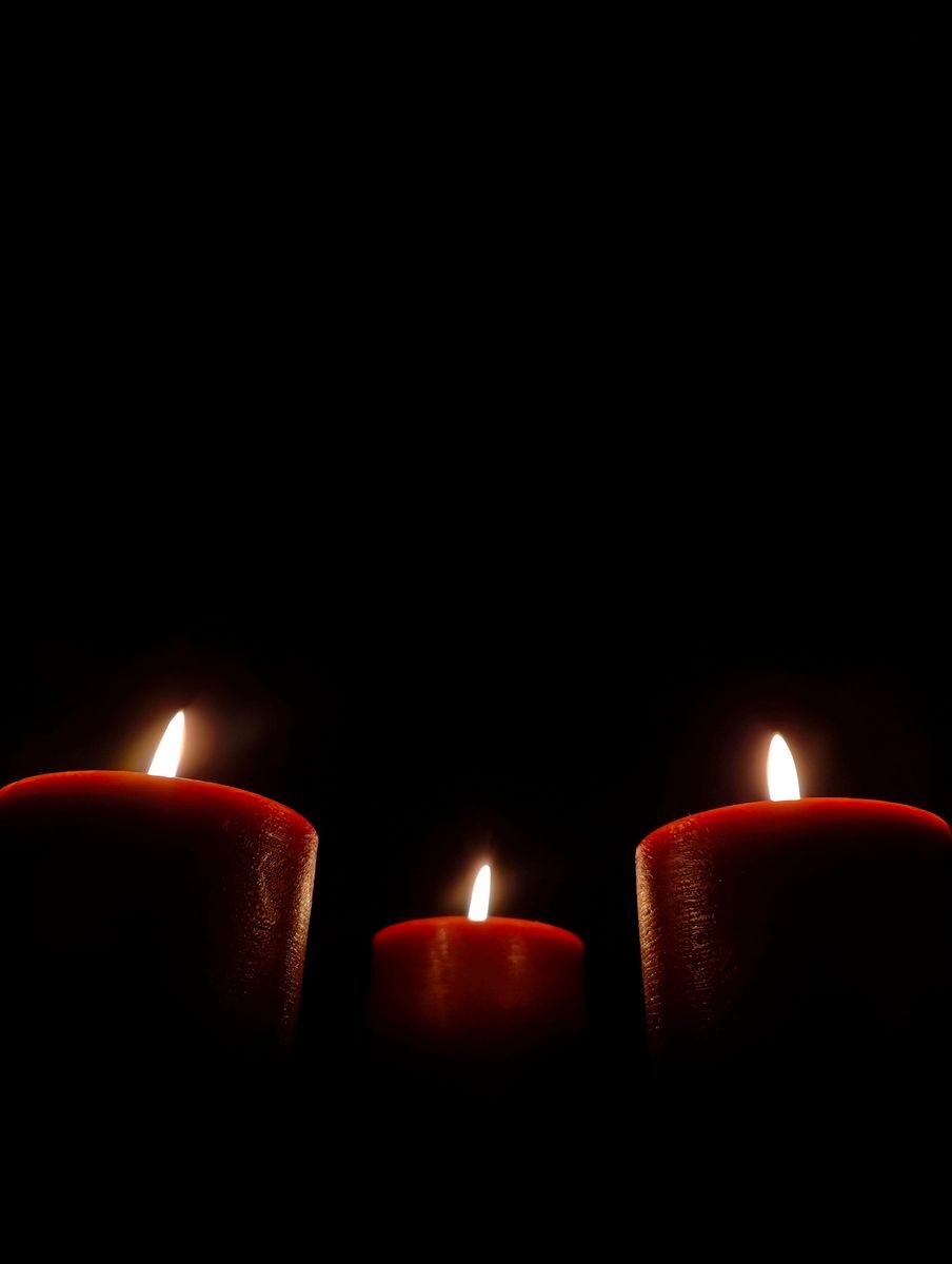 Moody and serene image of three red candles burning softly in the dark.